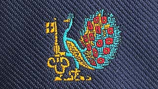 Close-up image of the embroidery of a turquoise, red and gold peacock holding a golden key, as per the University's coat of arms, taken from a University tie purchased in 1988.